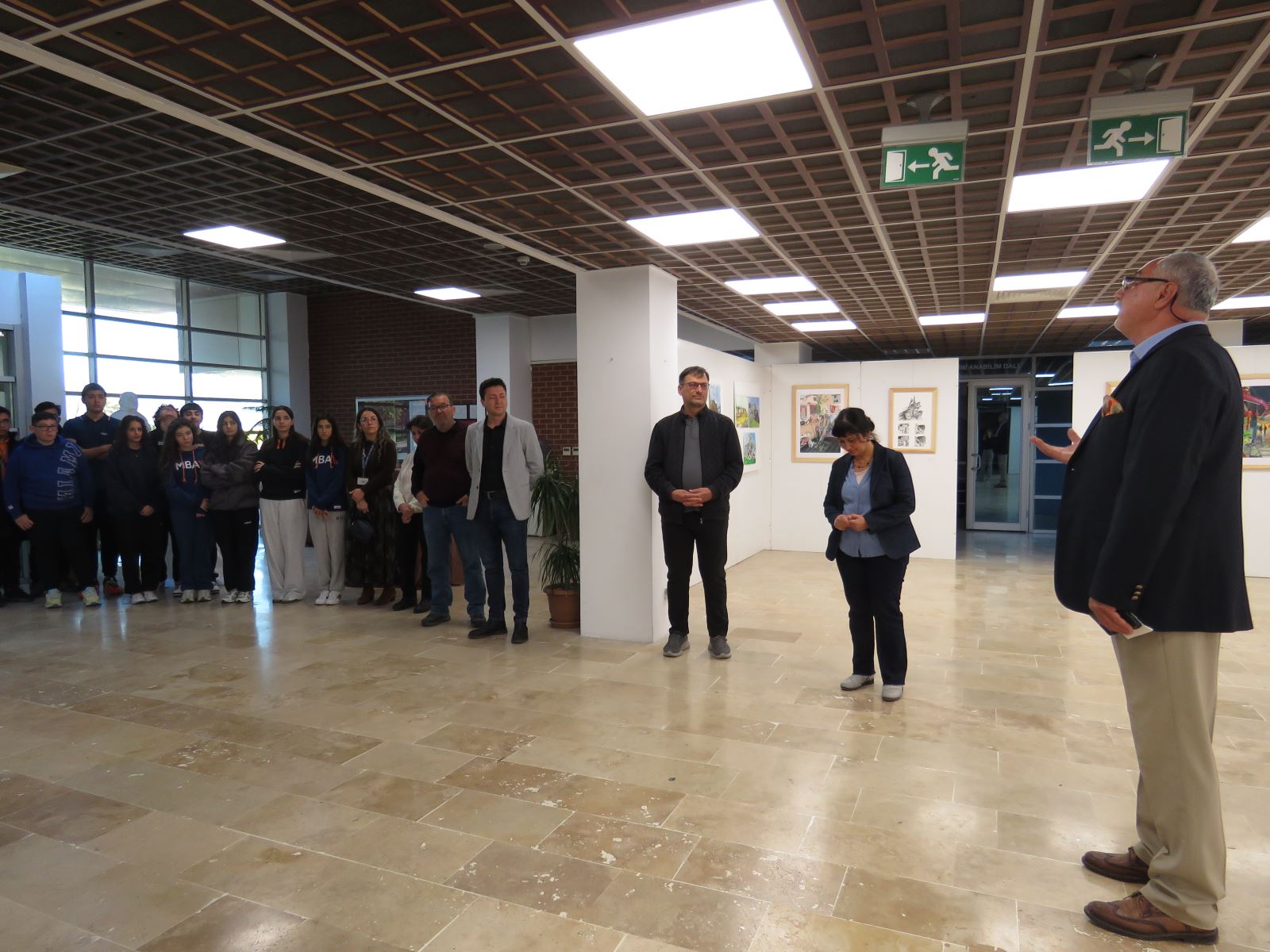 Sergi açılışında konuşmalar yapılıyor. Sergi salonunda öğrenciler ve akademisyenler görünmektedir.