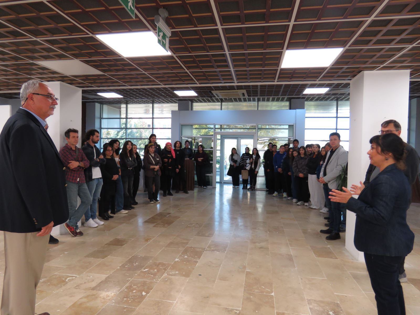 Sergi açılışında konuşmalar yapılıyor. Sergi salonunda öğrenciler ve akademisyenler görünmektedir.